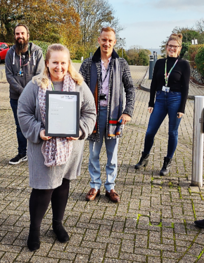 Foundever team, socially distant outside in car park holding their silver award